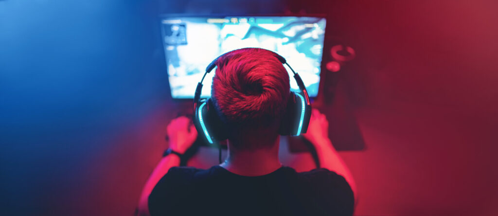 Professioneller Gamer sitzt vor Monitor mit Kopfhörern, spielt Turniere online am Computer.