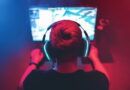 Professioneller Gamer sitzt vor Monitor mit Kopfhörern, spielt Turniere online am Computer.