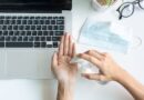 E-Learning Hygiene: Person desinfiziert Hände am Laptop-Arbeitsplatz mit Maske im Hintergrund
